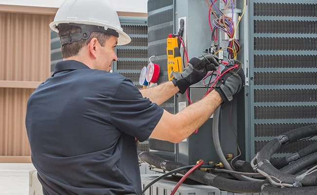 Technician checking electrical connections on an outdoor air conditioning unit
